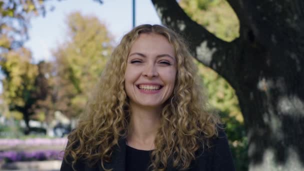 Esdoorn bladeren vallen op het hoofd van een jong mooi meisje in het park onder een boom — Stockvideo