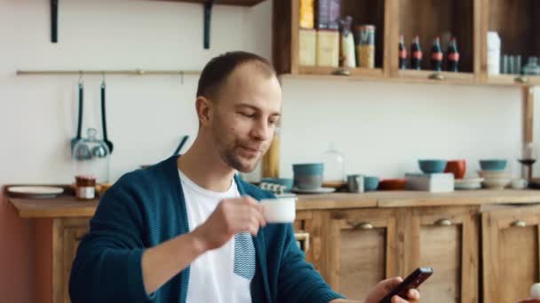 Man using phone while having cup of coffee in kitchen at home 4k — Stock Video