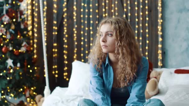 Vacker söt flicka sitter på sängen på bakgrunden av granen — Stockvideo