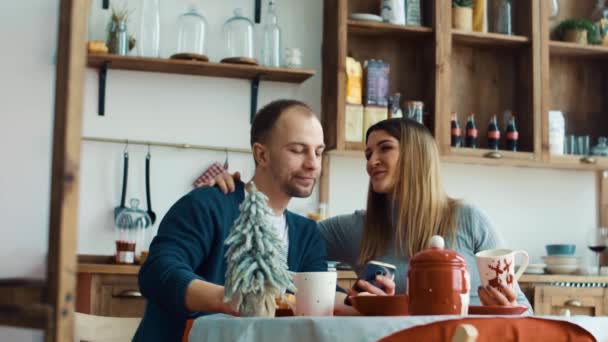 Беременные жена и муж завтракают на кухне со смартфоном — стоковое видео