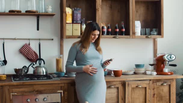 Έγκυος γυναίκα στην κουζίνα με smartphone — Αρχείο Βίντεο
