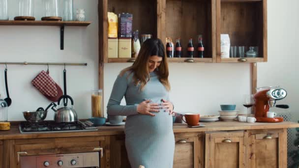 Mujer embarazada acariciando la barriga en la cocina temprano en la mañana — Vídeos de Stock