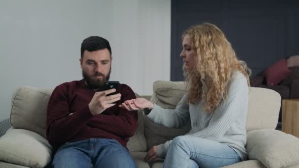 Мужчина с телефоном игнорирует свою девушку, сидящую на диване — стоковое видео