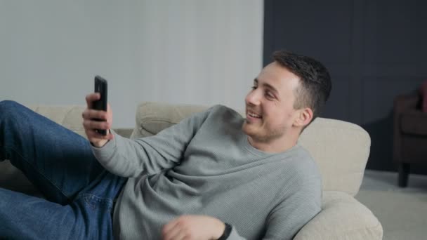 Man op het huis op Sofa liggen doet Video-oproep op Smartphone — Stockvideo