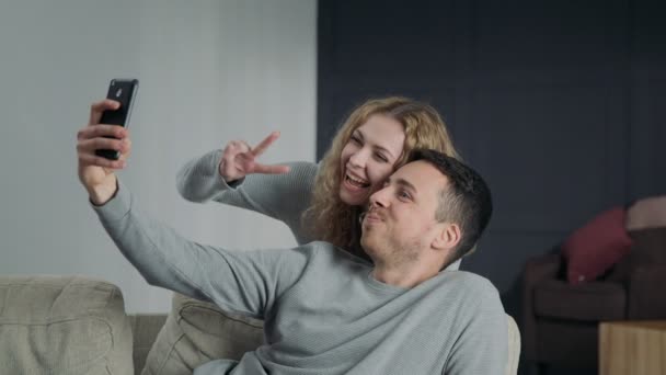 Pareja haciendo selfie en la cámara del teléfono inteligente, possing y sonriendo en casa — Vídeos de Stock