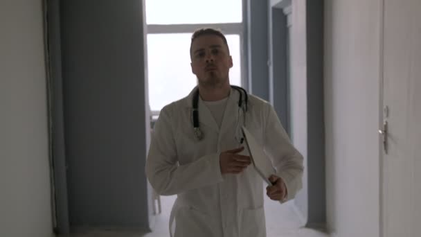 En läkare med stetoskop går genom korridoren av sjukhuset — Stockvideo