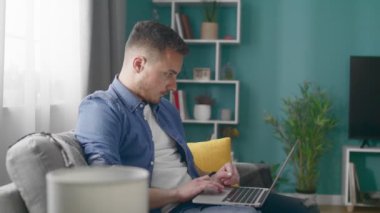 Young Man at Home Works on a Laptop Computer