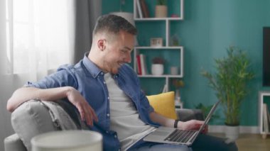 Young Man at Home Sitting on Sofa Does Video Call Using Laptop Computer