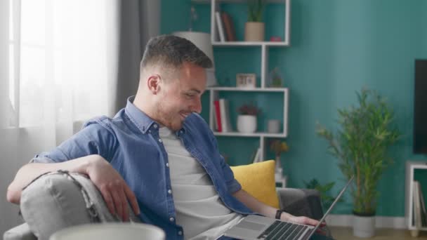 Attraktiv man hemma sitter på soffan gör video samtal med bärbar dator — Stockvideo