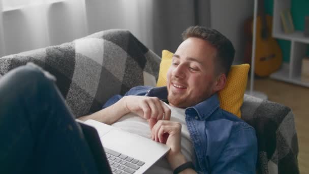 Uomo attraente a casa sdraiato sul divano fa videochiamata utilizzando computer portatile — Video Stock