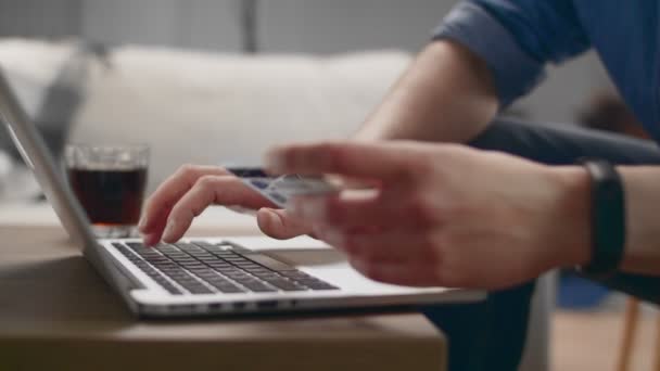 CloseUp tiro de homem em casa ele detém cartão de crédito e tipos de número em laptop — Vídeo de Stock