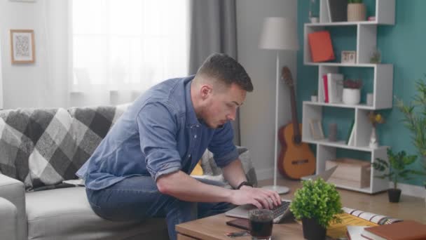 Молодой человек с ноутбуком звонит на смартфон дома — стоковое видео