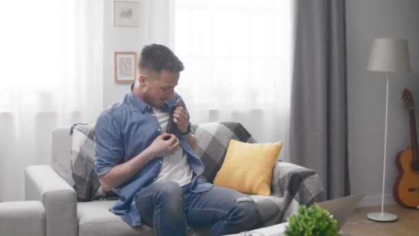 Knappe man speelt een onzichtbare gitaar met een tv-afstandsbediening in zijn hand — Stockvideo