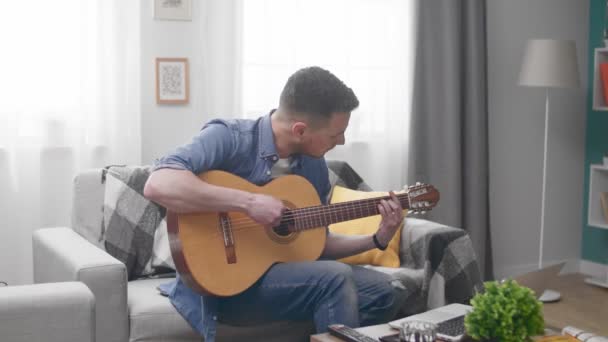 Hombre guapo aprende a tocar la guitarra con la ayuda de un tutorial en línea — Vídeo de stock