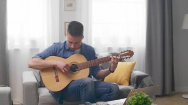 Yakışıklı adam kanepede evde akustik gitar çalıyor