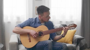 Yakışıklı adam kanepede evde akustik gitar çalıyor