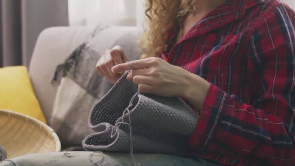 Zoom out of young woman sitting on couch and knitting in home — ストック動画
