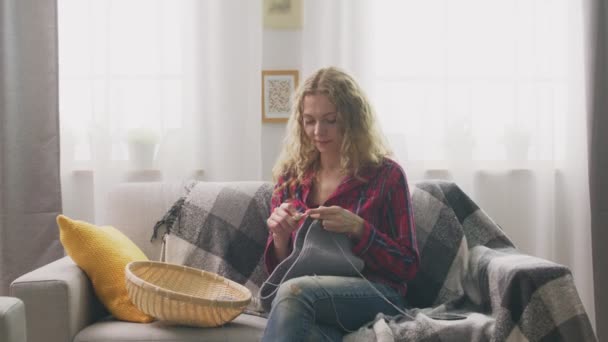 Zoom in van vrouw zitten op de bank en breien in huis en kijken in de camera — Stockvideo