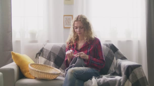 Vergrößerung einer Frau, die auf dem Sofa sitzt, zu Hause strickt und in die Kamera schaut — Stockvideo