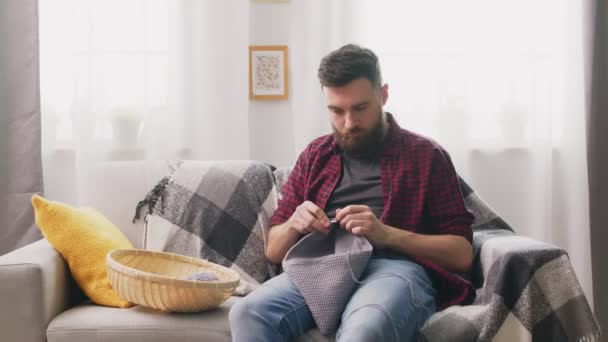 Porträt eines Mannes, der zu Hause auf dem Sofa sitzt und strickt — Stockvideo