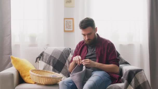 Férfi ül a kanapén, és kötés otthonos otthon — Stock videók