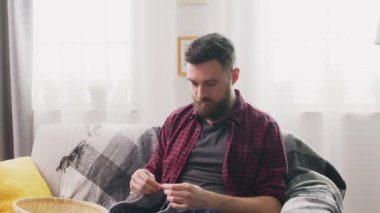 Zoom in of man sitting on sofa and knitting at home
