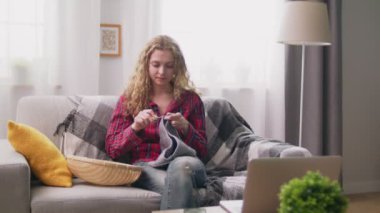 Kanepede oturan ve rahat evde tığ işi giysiler ören kadının el çekim