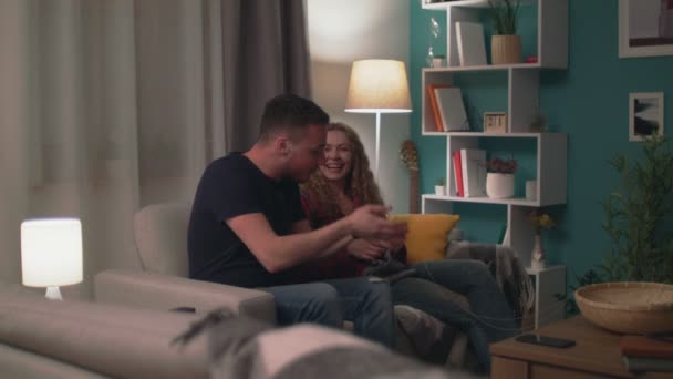 Panning of young happy couple sitting on sofa have fun chatting and laughing — Stock Video