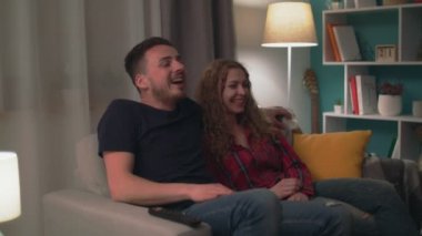 Akşam oturma odasında bir komedi izlerken çift gülüyor el çekim