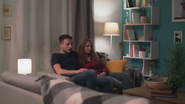 Zoom in shot of Young couple on sofa late at night watching a scary horror film — Stock Video