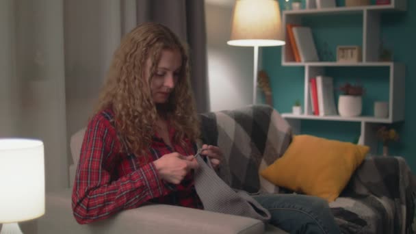 Toma de mano de la mujer sentada en el sofá y tejiendo por la noche — Vídeo de stock