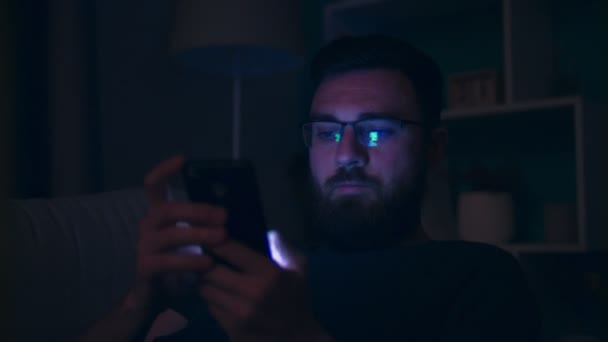 Średni strzał w średnim wieku człowiek siedzi na kanapie używa smartphone wieczorem — Wideo stockowe