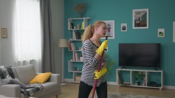 Jeune femme lave le sol dans l'appartement et chante une chanson dans la serpillière comme un microphone — Video