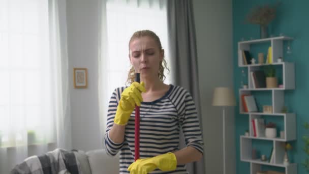 Handbild einer jungen Frau, die ein Lied singt und dabei einen Wischmopp als Mikrofon benutzt — Stockvideo