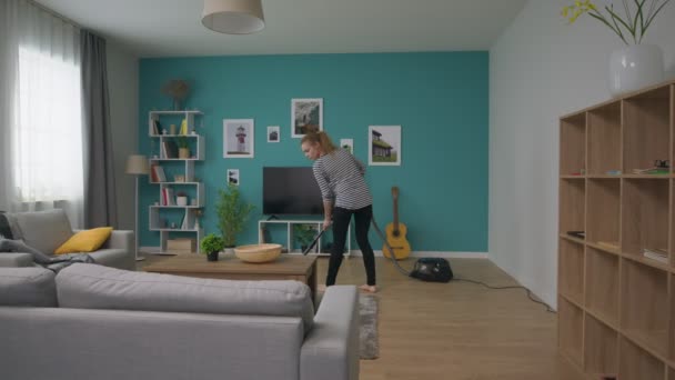 Panning de jovem mulher bonita aspirando seu aconchegante apartamento — Vídeo de Stock