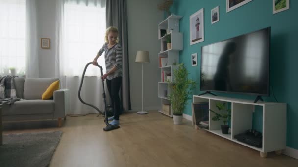 Портативный снимок молодой красивой девушки пылесосит свою уютную гостиную — стоковое видео