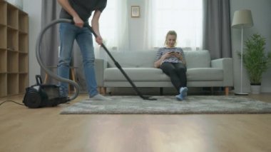 Parke zemin vakumlama Adam ve kanepede akıllı telefon kullanarak kız arkadaşı