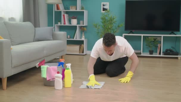 Mann fühlt sich müde, wenn er nach dem Putzen zu Hause auf Holzboden im Wohnzimmer sitzt — Stockvideo