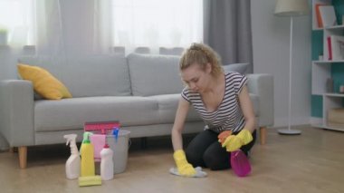 Sarı eldivenli genç bir kadın. Oturma odasında yerde bez temizliyor.