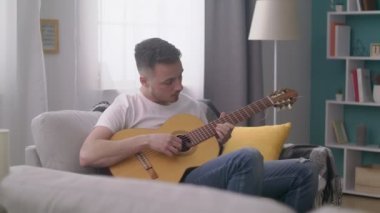Genç adamın takibi rahat oturma odasında gitar çalar.