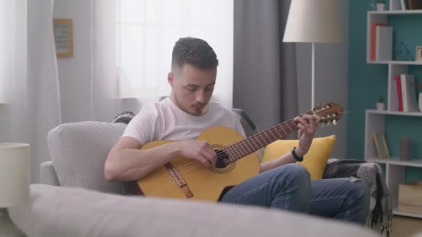 Η μετατόπιση του νεαρού άντρα παίζει κιθάρα στο άνετο σαλόνι του. — Αρχείο Βίντεο