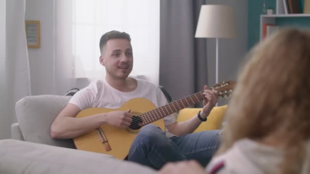 Η μετατόπιση του ανθρώπου παίζει την κιθάρα για τους φίλους του σε ένα άνετο σαλόνι. — Αρχείο Βίντεο