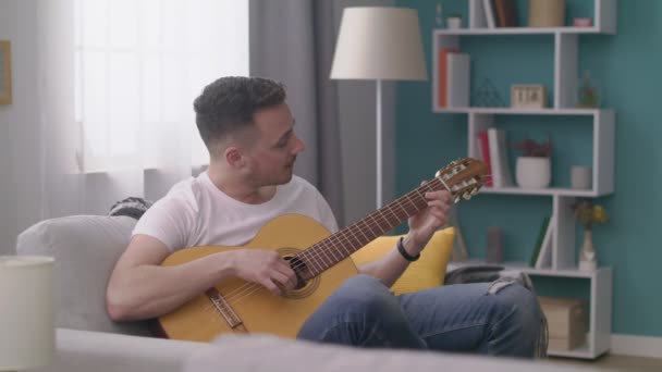 Rastreamento de homem toca guitarra para seus amigos em uma sala de estar aconchegante . — Vídeo de Stock