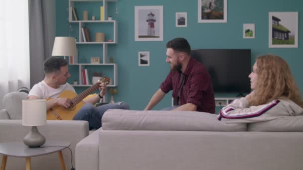 Ampio colpo di uomo suona la chitarra per i suoi amici in un accogliente soggiorno . — Video Stock