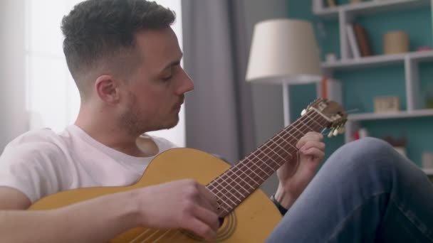 Handheld tiro de homem toca guitarra em sua acolhedora sala de estar . — Vídeo de Stock