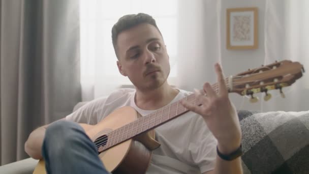 Handheld tiro de homem bonito toca guitarra em sua acolhedora sala de estar . — Vídeo de Stock