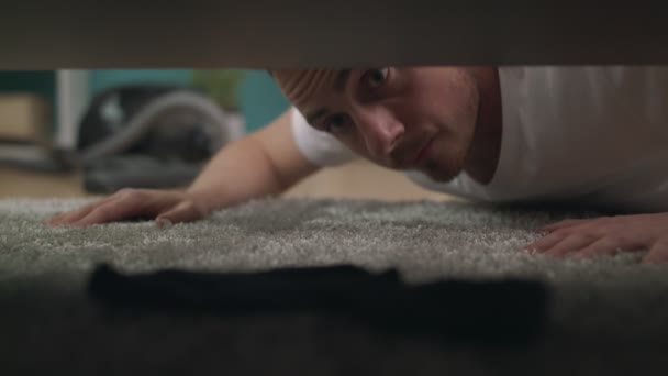 A young guy finds a lost sock under the sofa in the living room — Stock Video