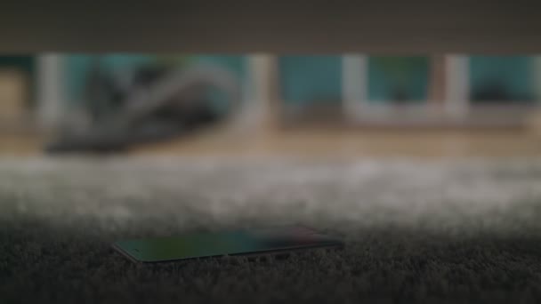 A young guy finds a lost smartphone under the sofa in the living room — Stock Video