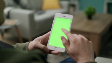 Oturma odasında yeşil ekranlı bir telefon kullanan erkek eller