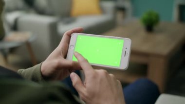Bir adam oturma odasında yeşil ekran ile bir akıllı telefon bir karakter seçer